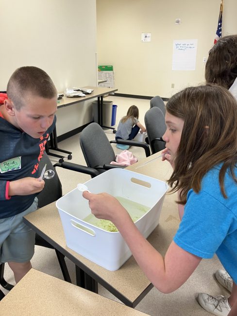 An ambassador helps a younger member look for water critters at Super Saturday.
